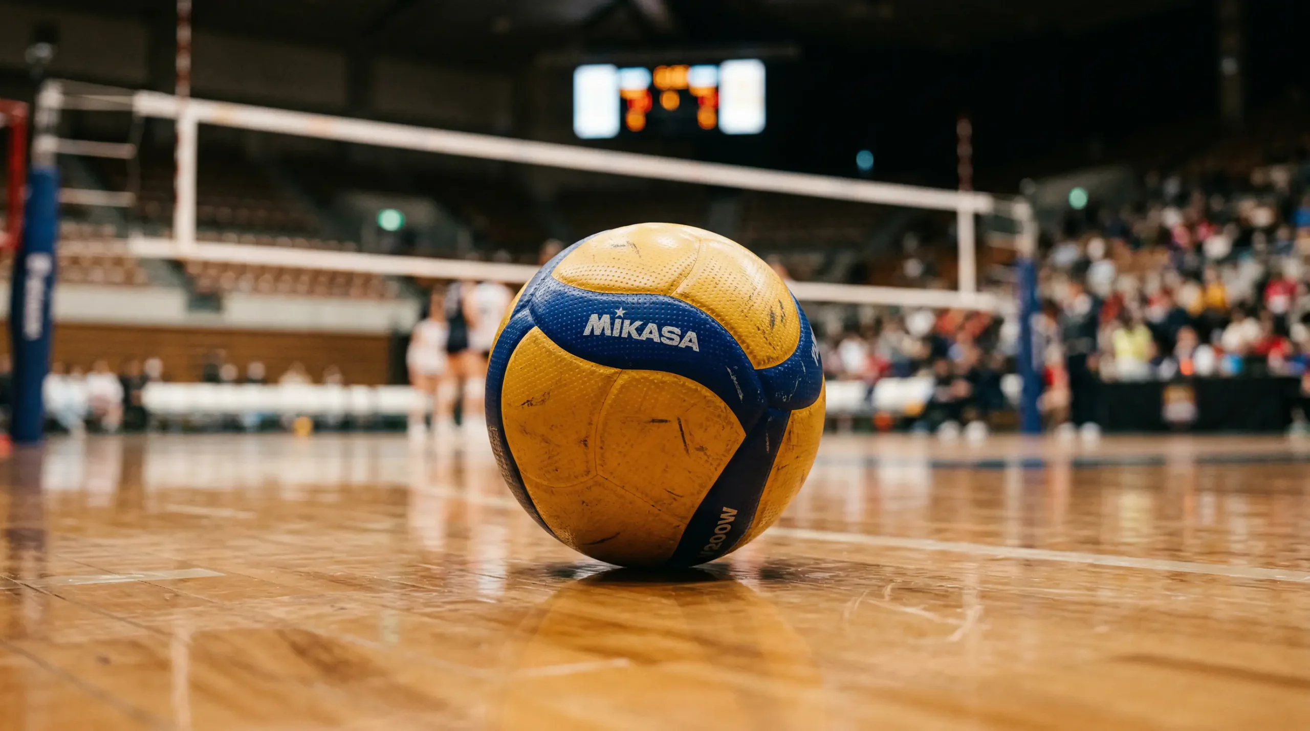 Nahaufnahme eines Volleyball auf dem Hallenboden mit Spielfeld im Hintergrund