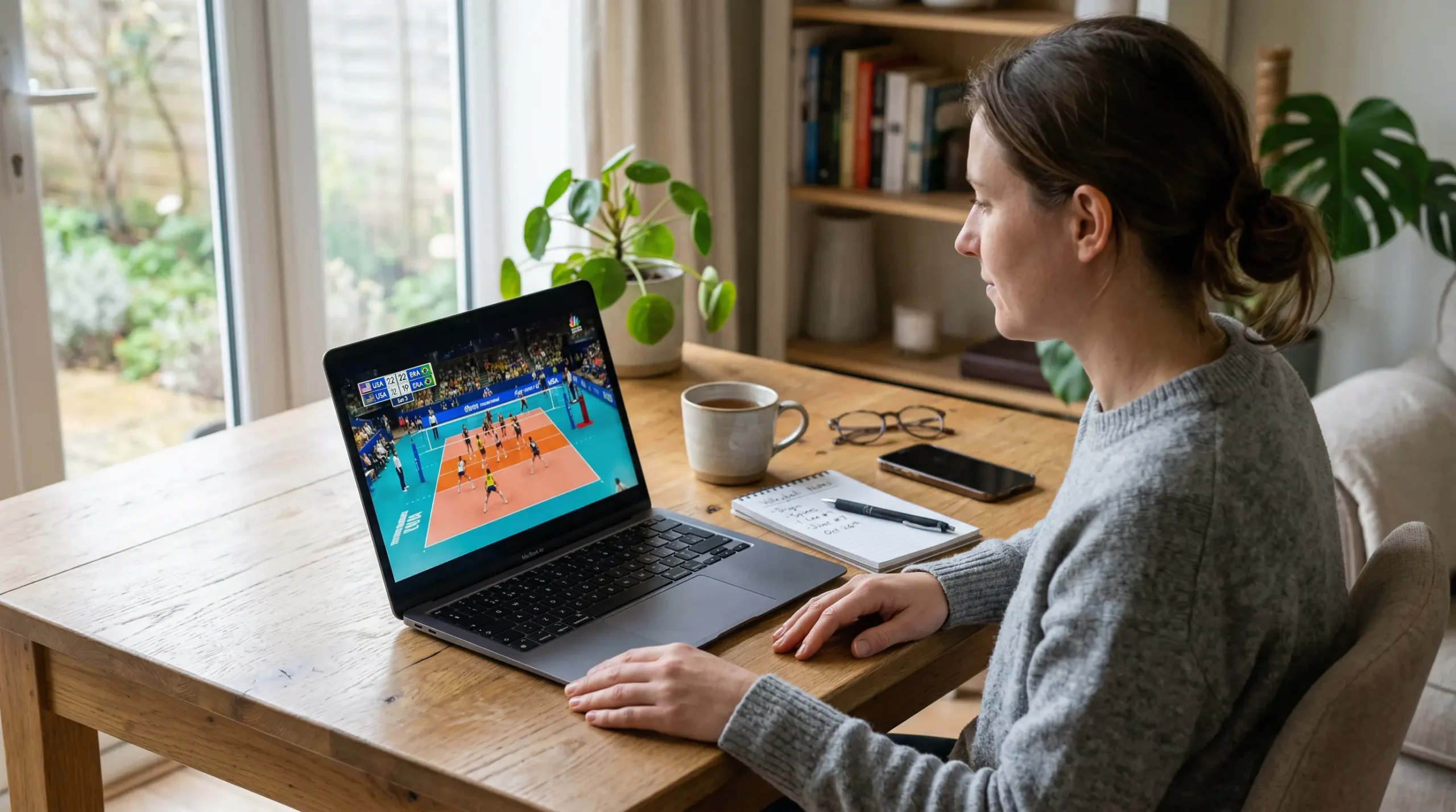 Person schaut ein Volleyball-Spiel auf dem Laptop mit Notizblock daneben
